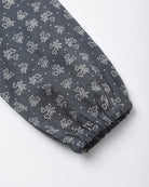 A close-up of a dark gray fabric sleeve or cuff with an all-over white bow and bow print pattern, finished with a gathered elastic hem.