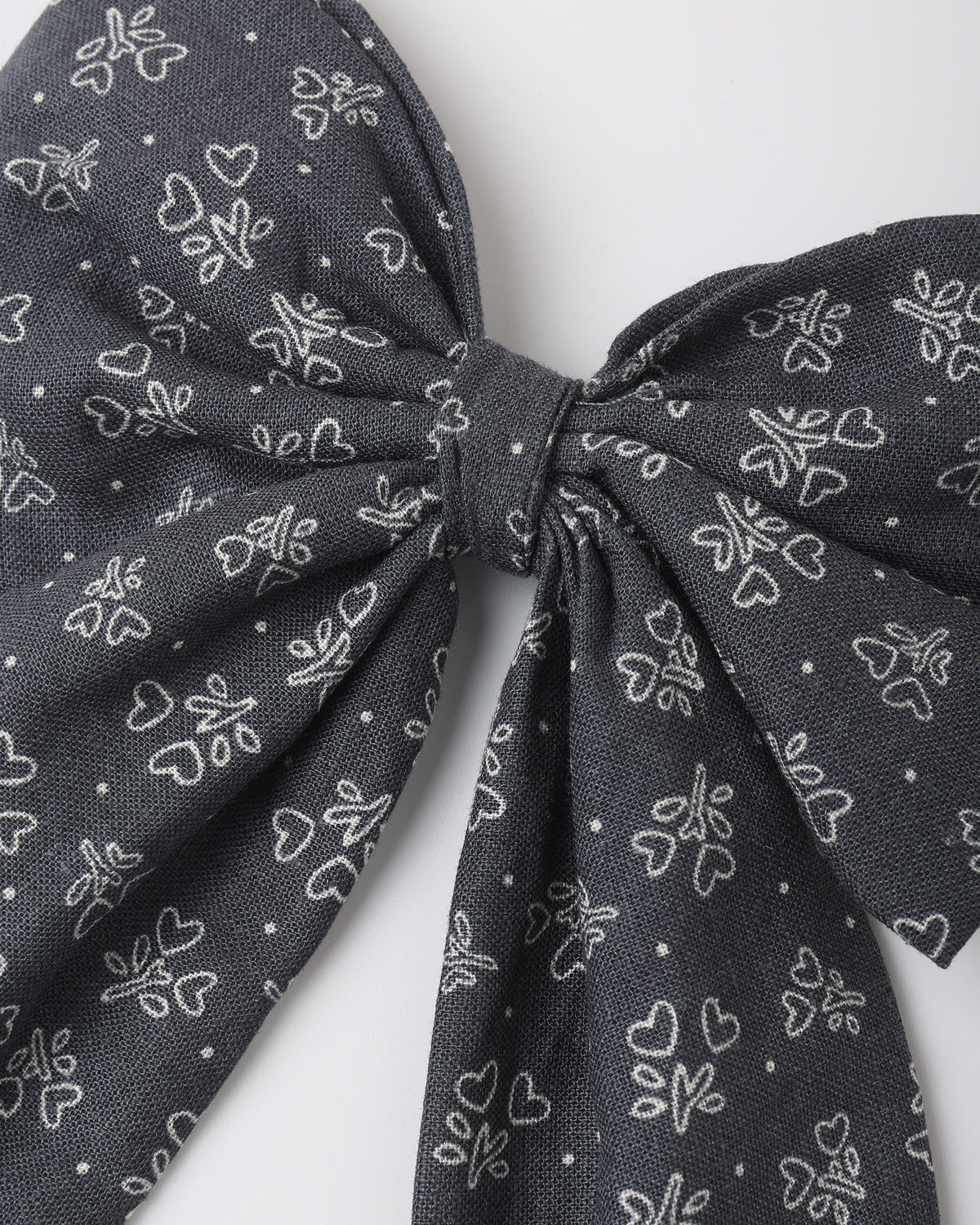 A close-up of a dark gray fabric bow with a white line-art pattern of small hearts and floral motifs, set against a plain light gray background.