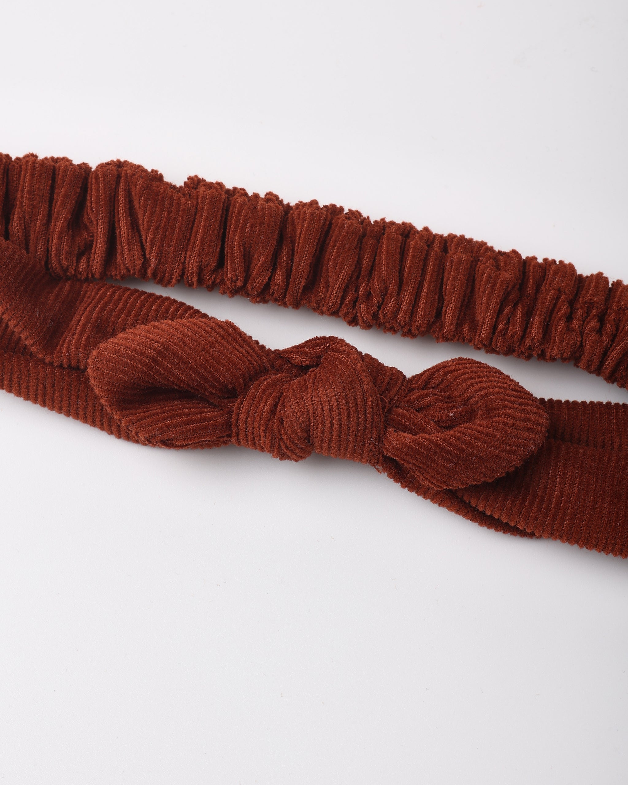 A rust-brown corduroy headband with a knotted bow detail and a matching elastic band, displayed on a clean white background.