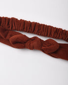 A rust-brown corduroy headband with a knotted bow detail and a matching elastic band, displayed on a clean white background.