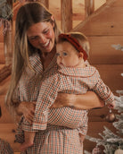 A baby wearing plaid pajamas and a rust-brown corduroy headband with a knotted bow detail.