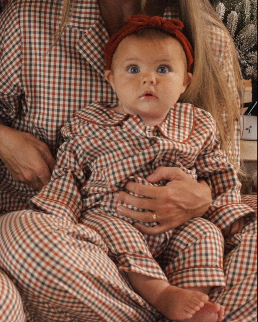 A baby wearing plaid pajamas and a rust-brown corduroy headband with a knotted bow detail.