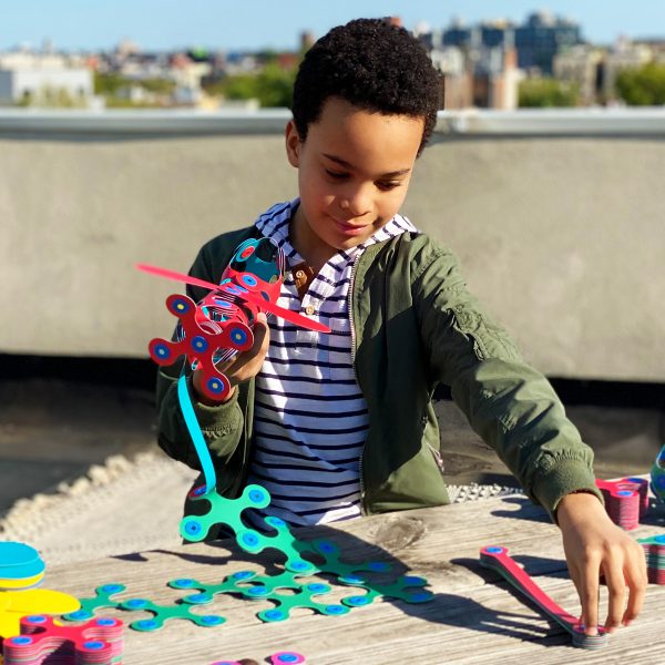 A young boy colorful Clixo magnetic play set with packaging on a biege background
