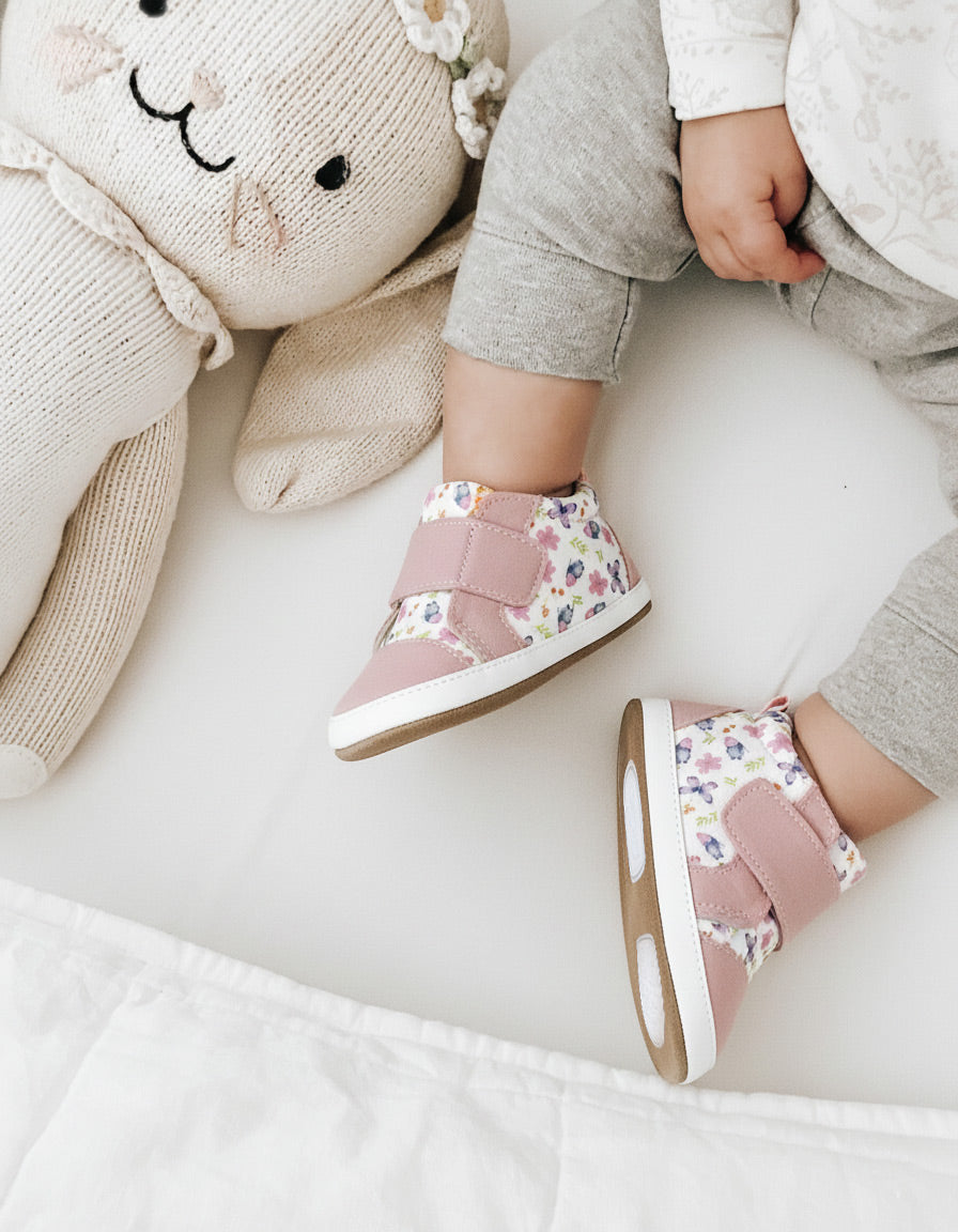 Child wearing pink floral shoes with a soft toy on a white surface