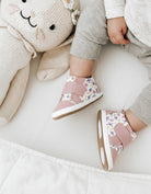 Child wearing pink floral shoes with a soft toy on a white surface