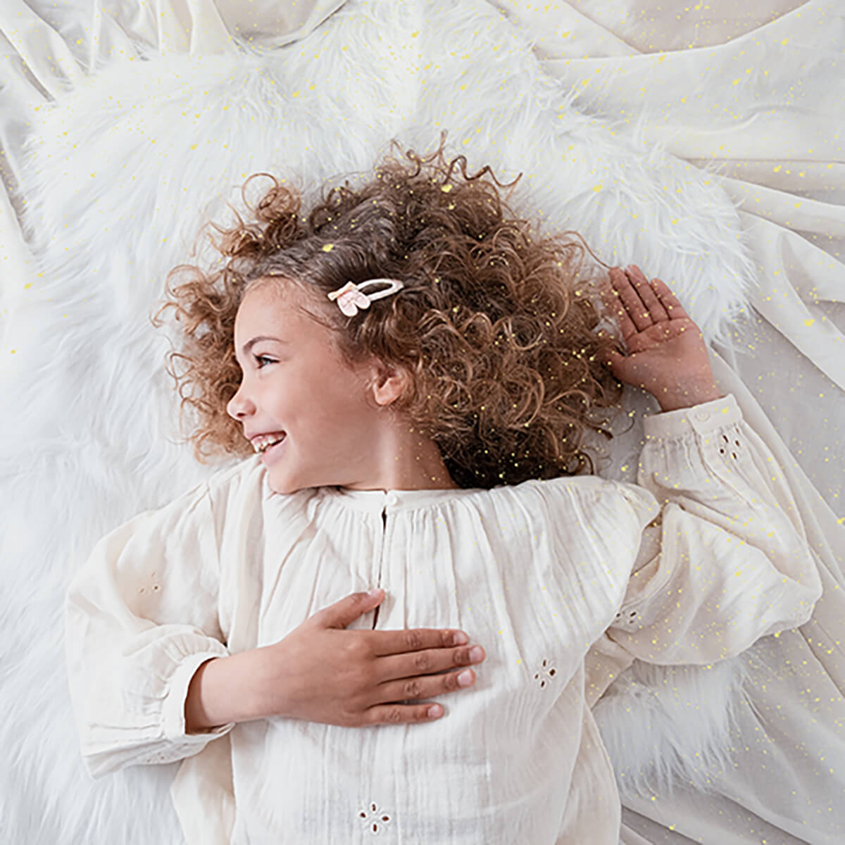 Young girl with curly hair lying on a fluffy white surface