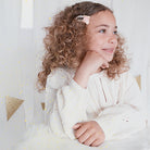 Young girl with curly hair wearing a white outfit with gold polka dots, sitting on a light-colored couch.
