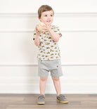 Child wearing a striped shirt and gray shorts holding a toy against a white wall.