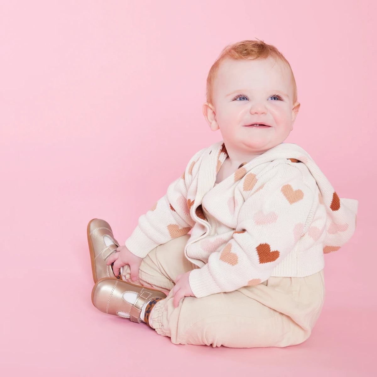 Baby wearing a heart-patterned outfit on a pink background