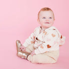 Baby wearing a heart-patterned outfit on a pink background