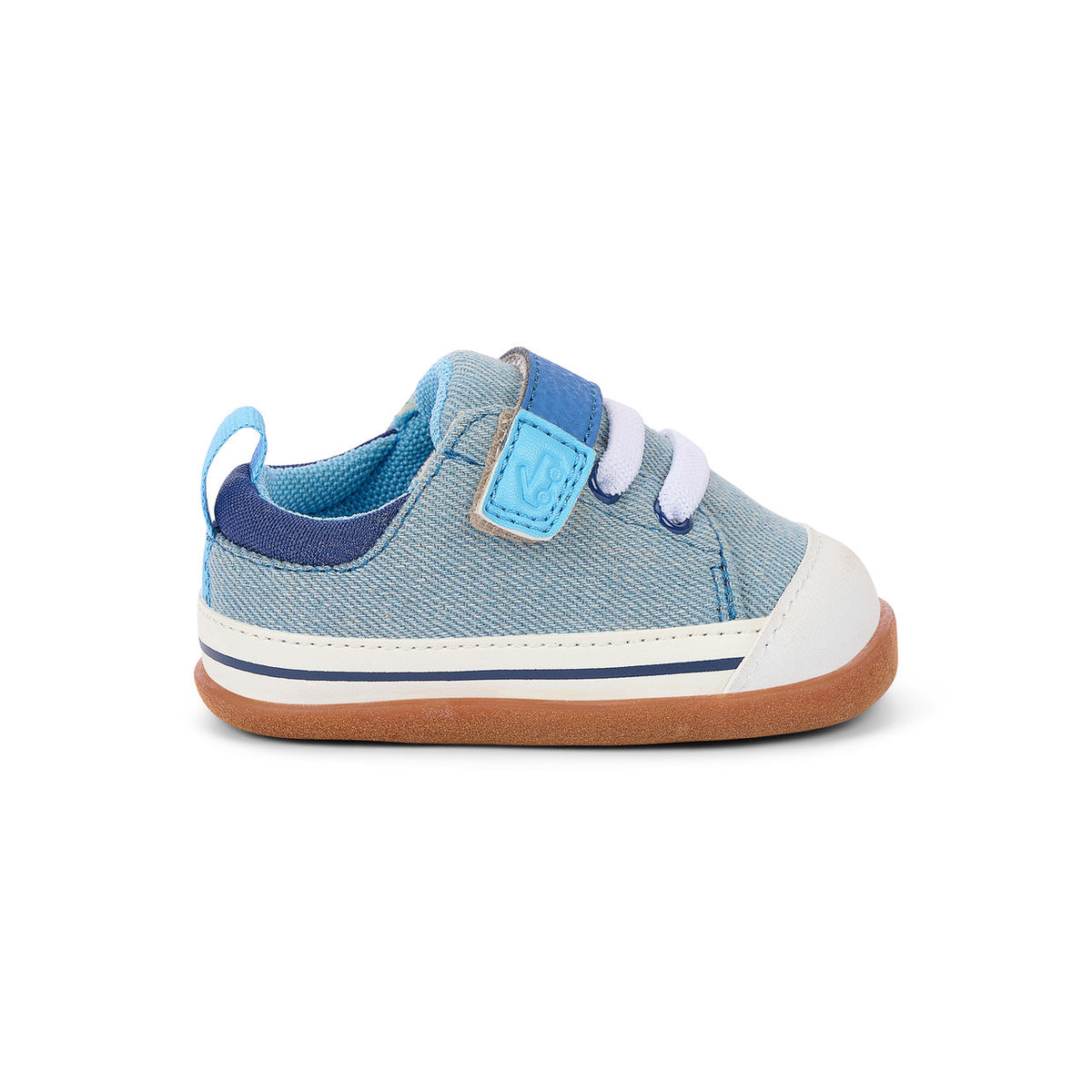 A single toddler sneaker in light blue denim canvas with a dark blue collar, a light blue hook-and-loop strap closure, white laces, a white rubber toe cap, and a brown flexible sole, shown from a side profile on a white background.