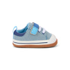 A single toddler sneaker in light blue denim canvas with a dark blue collar, a light blue hook-and-loop strap closure, white laces, a white rubber toe cap, and a brown flexible sole, shown from a side profile on a white background.