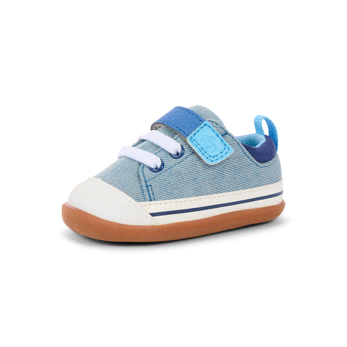 A single toddler's canvas shoe in light blue denim-like fabric, featuring a white rubber toe cap, white laces, a light blue hook-and-loop strap, a dark blue heel pull tab, and a brown gum sole, shown against a plain white background.