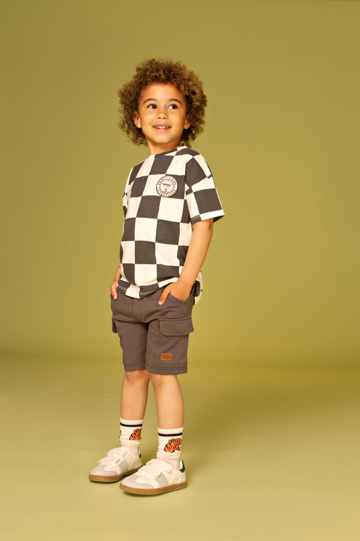 Child wearing a checkered shirt and cargo shorts on a solid background