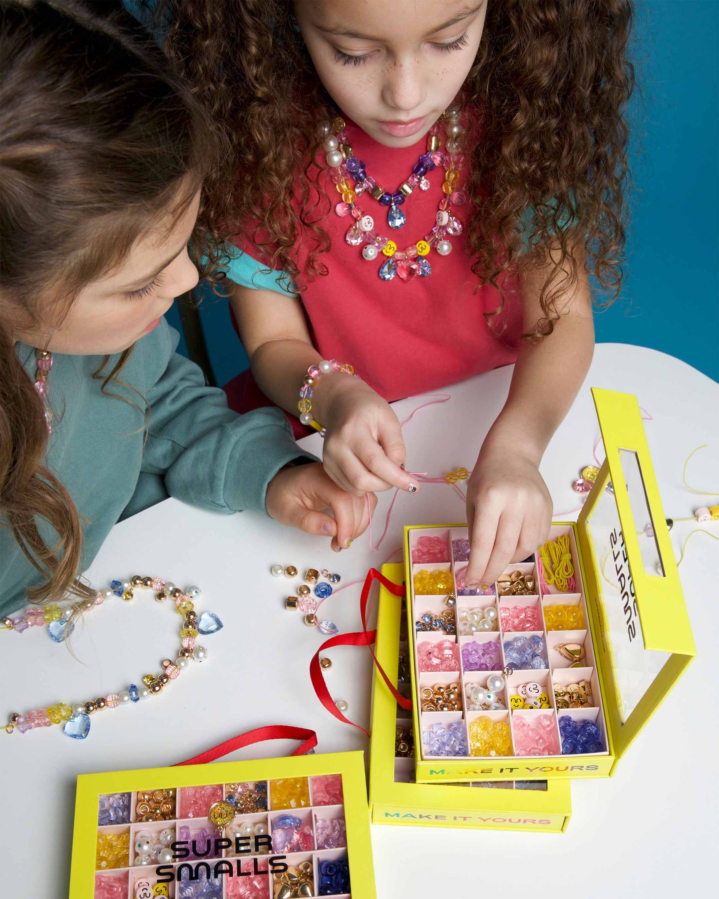 Two children playing with a jewelry-making kit on a table.