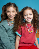Two young girls wearing colorful necklaces against a blue background