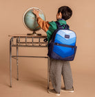 Child with a blue backpack looking at a globe on a desk against a beige background