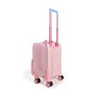 Rear three-quarters view of a pink State Bags Mini Logan carry-on suitcase designed to look like a house, showcasing its blue telescopic handle, 360-degree spinner wheels, and side details against a transparent background.