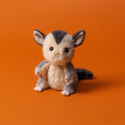 Stuffed animal toy resembling a small creature with a striped head on an orange background