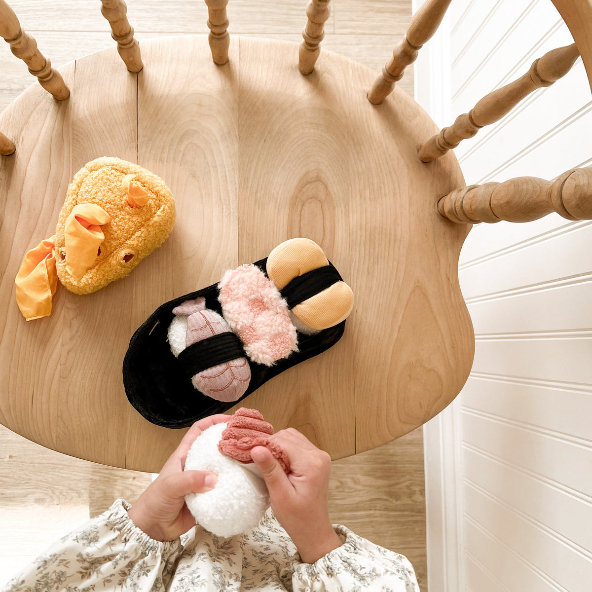 Pair of cartoon slippers on a wooden chair with a person holding a plush toy.