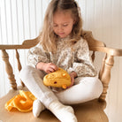Young girl sitting on a wooden chair holding a yellow teddy bear.