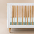 White crib with wooden slats and a light green mattress against a beige background