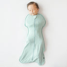 Baby sleeping in a light green swaddle on a white background