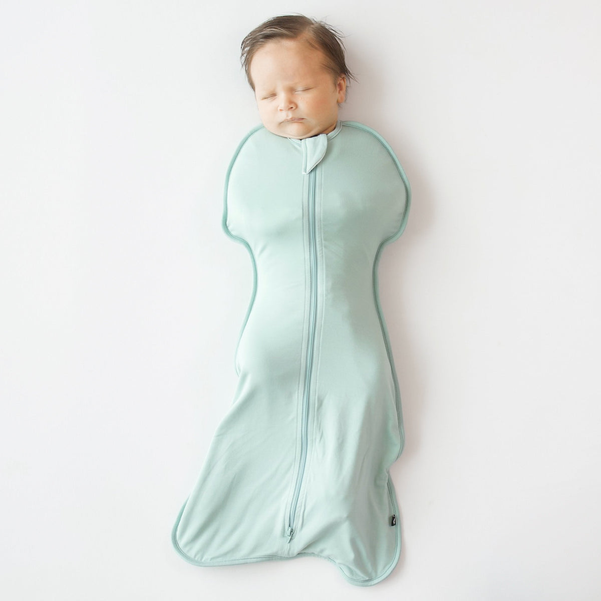 Baby sleeping in a light green swaddle on a white background