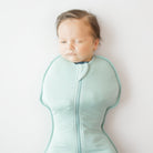 Baby sleeping in a light blue sleep bag with a white background