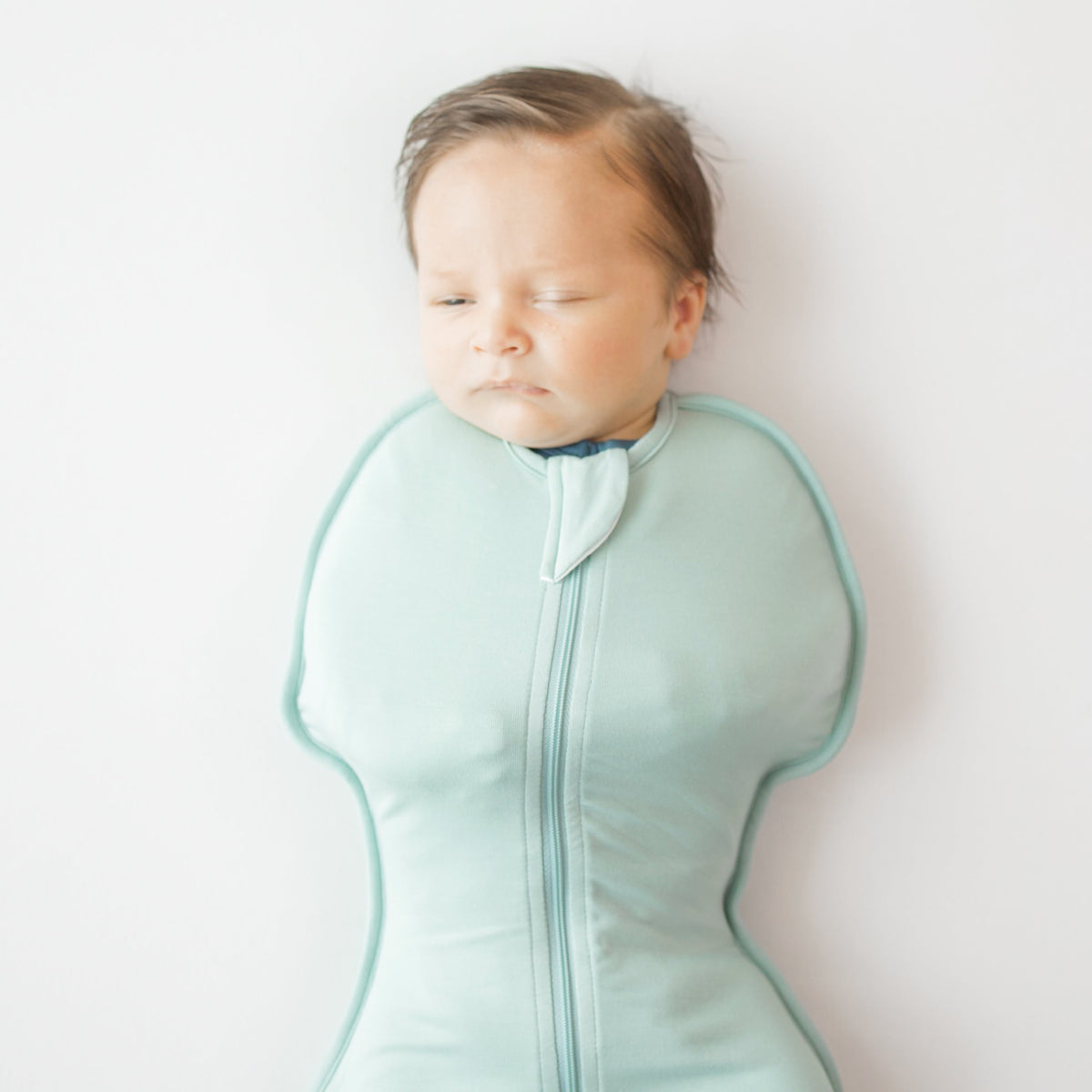 Baby sleeping in a light blue sleep bag with a white background