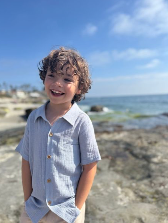 Child standing on a rocky beach with ocean and clear sky in the background