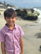 Child in a pink checkered shirt standing on a beach with ocean waves in the background