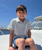 Child sitting on a boat deck with a clear blue sky background