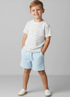 Young boy wearing a striped shirt and light blue shorts on a plain background