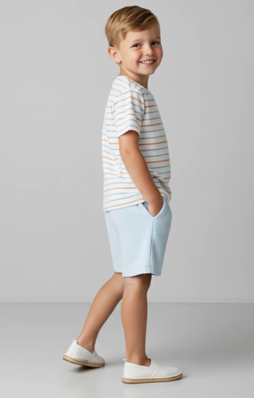 Young boy wearing a striped shirt and light shorts on a plain background