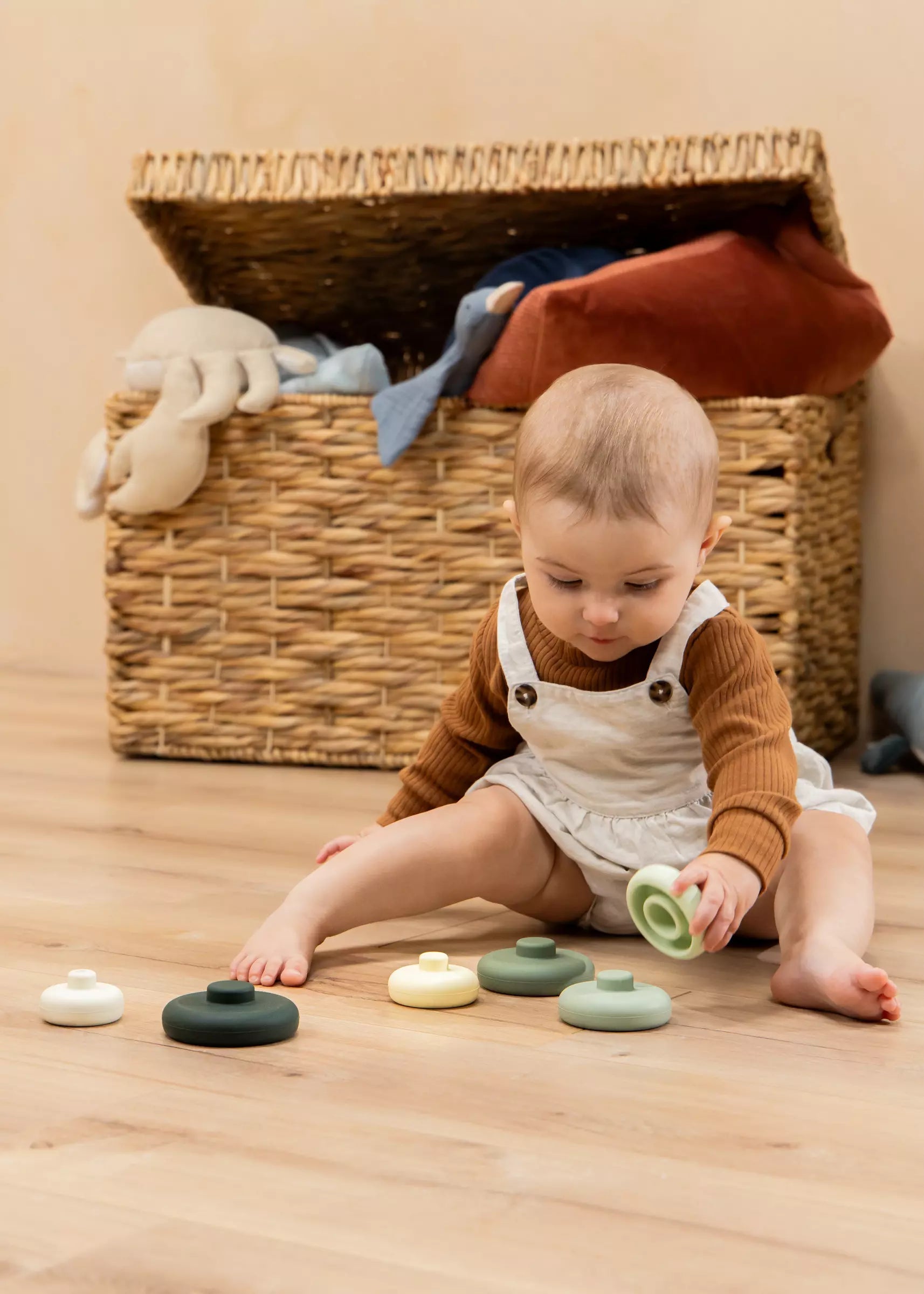 Baby playing with colorful toys on a wooden floor next to a wicker basket.