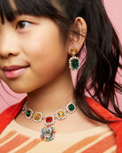 Close-up of a young girl wearing colorful gemstone jewelry against a pink background