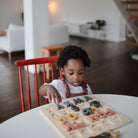 A toddler sitting at a table in a bright room, focused on placing a piece into a wooden alphabet puzzle.