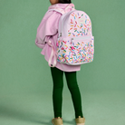 Person wearing a pink backpack with colorful sprinkles pattern on a green background