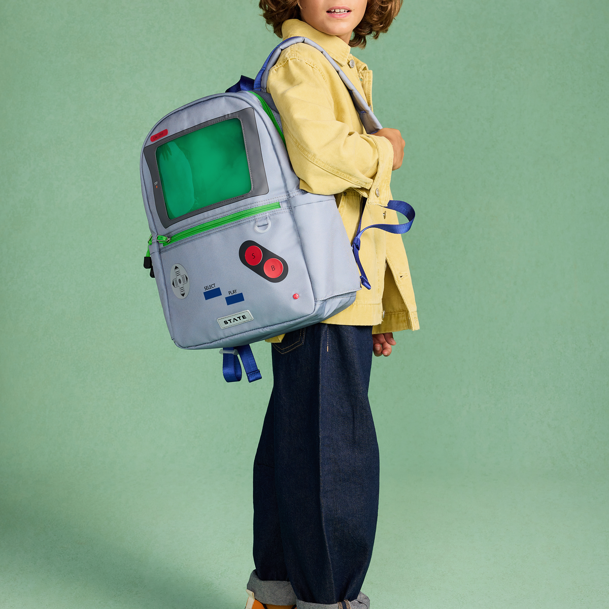 Child wearing a backpack designed like a vintage video game console against a green background