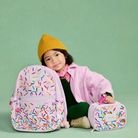 Child with a pink backpack and suitcase featuring colorful patterns on a green background