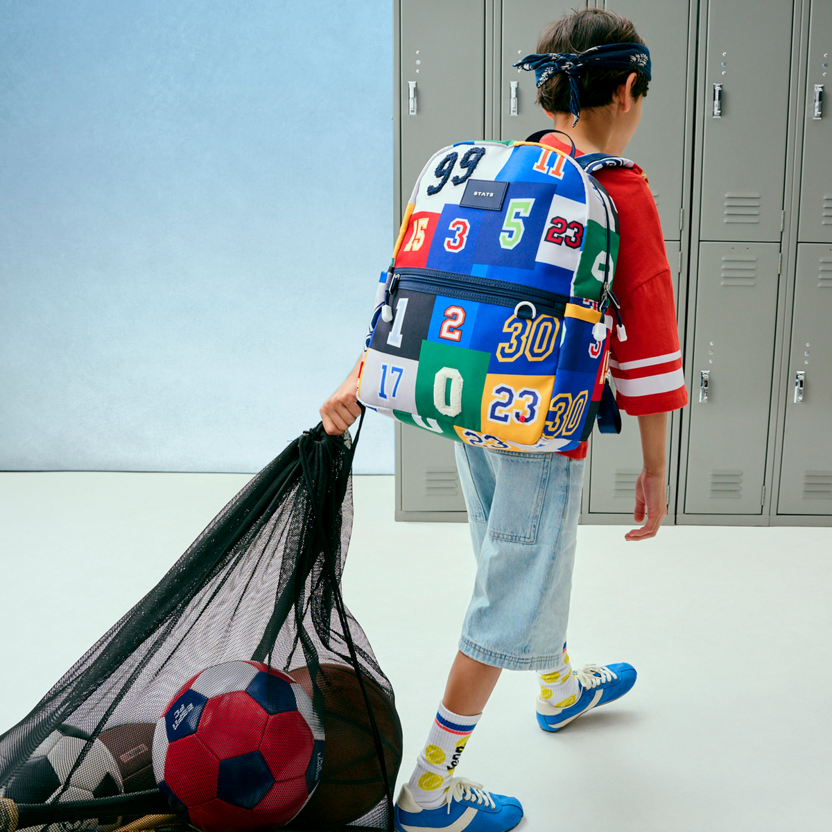 Person with a colorful backpack holding a soccer ball in a locker room.