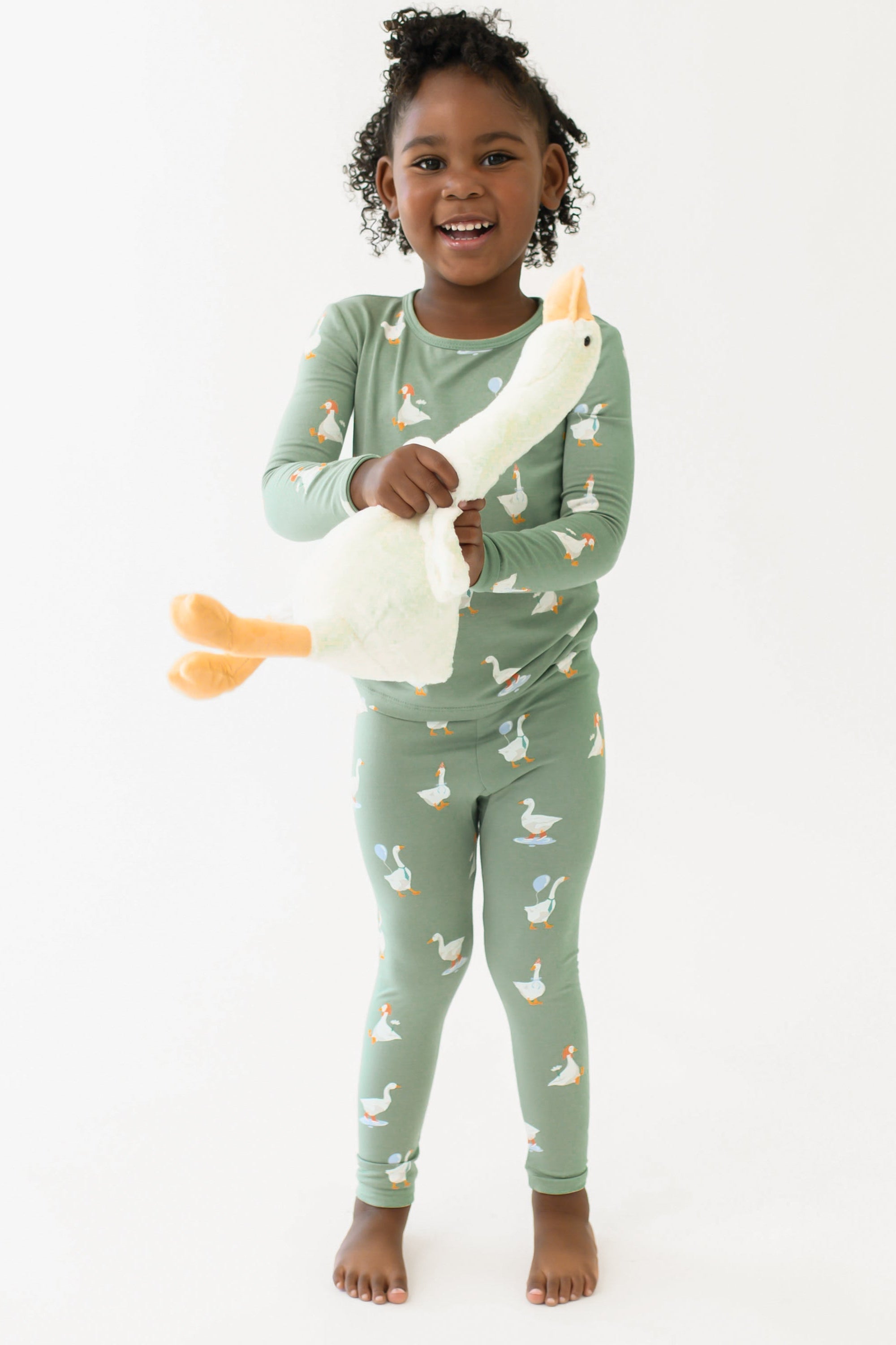 Child wearing green pajamas with duck pattern holding a plush toy, standing against a white background
