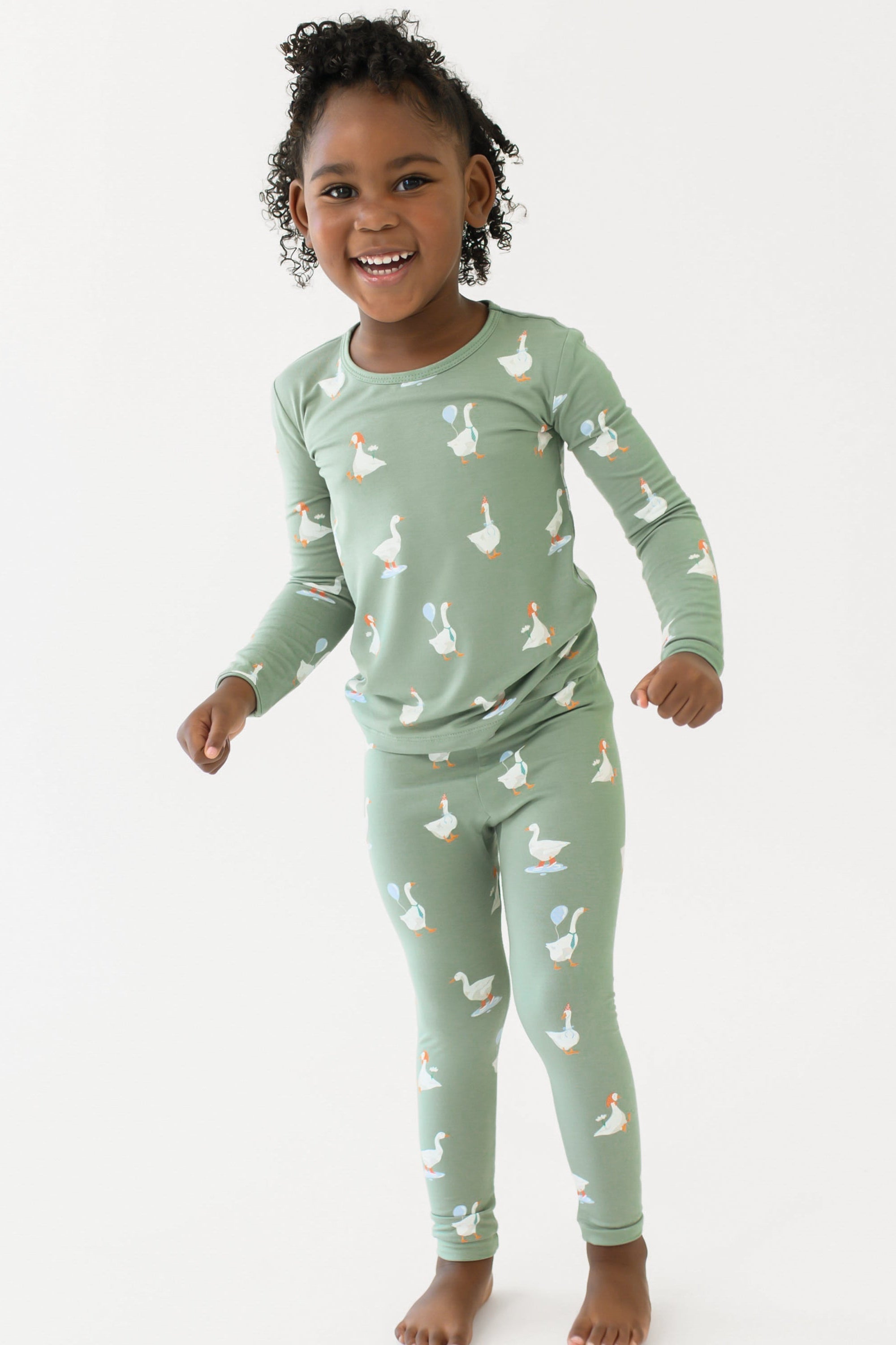 Child wearing a green pajama set with duck pattern on a white background