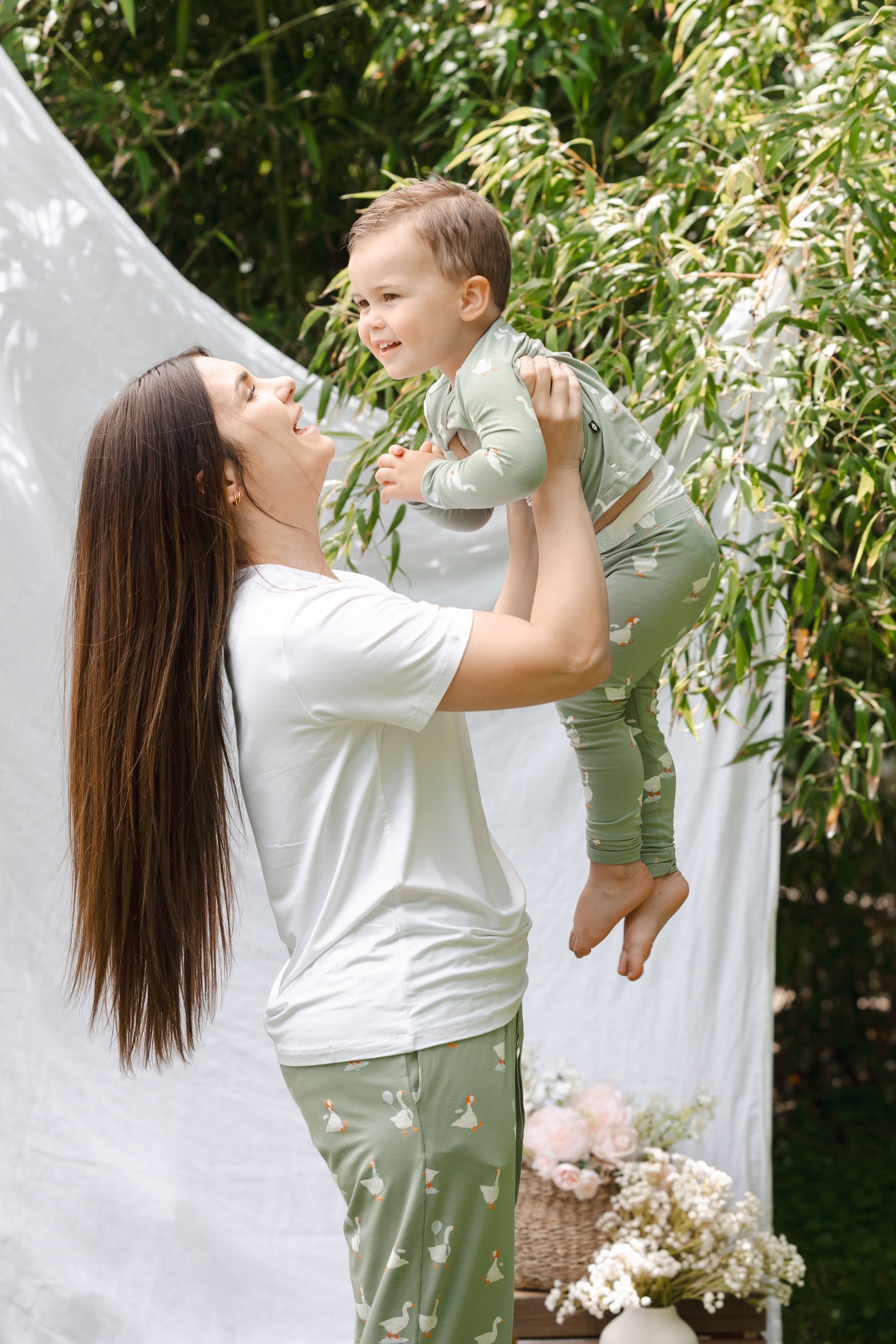 Woman holding a child outdoors with greenery and flowers in the background