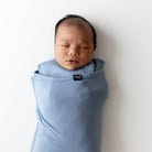 Newborn baby wrapped in a blue swaddle with a visible brand label on a white background