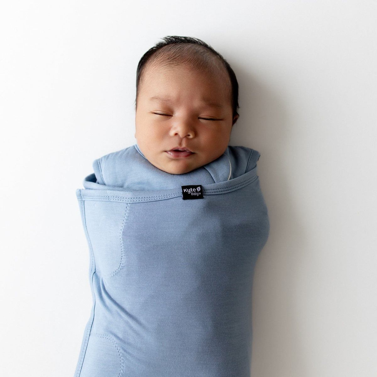 Newborn baby wrapped in a blue swaddle with a visible brand label on a white background