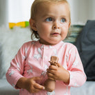 Child in pink pajamas holding a wooden toy in a room with toys in the background