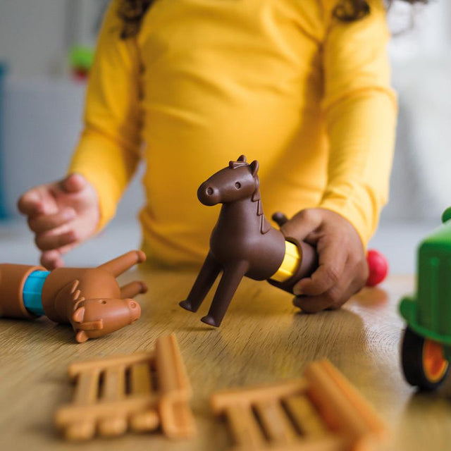 A child’s hands playing on the floor with pieces from the Smartmax My First Farm Tractor set, connecting a brown toy horse to a magnetic bar.