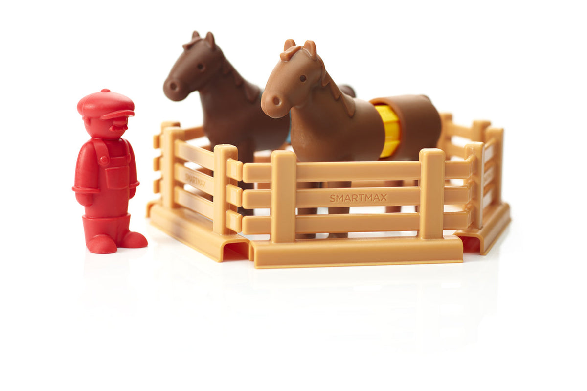 Two brown toy horses standing inside a wooden-look fenced enclosure, accompanied by a red farmer figure.